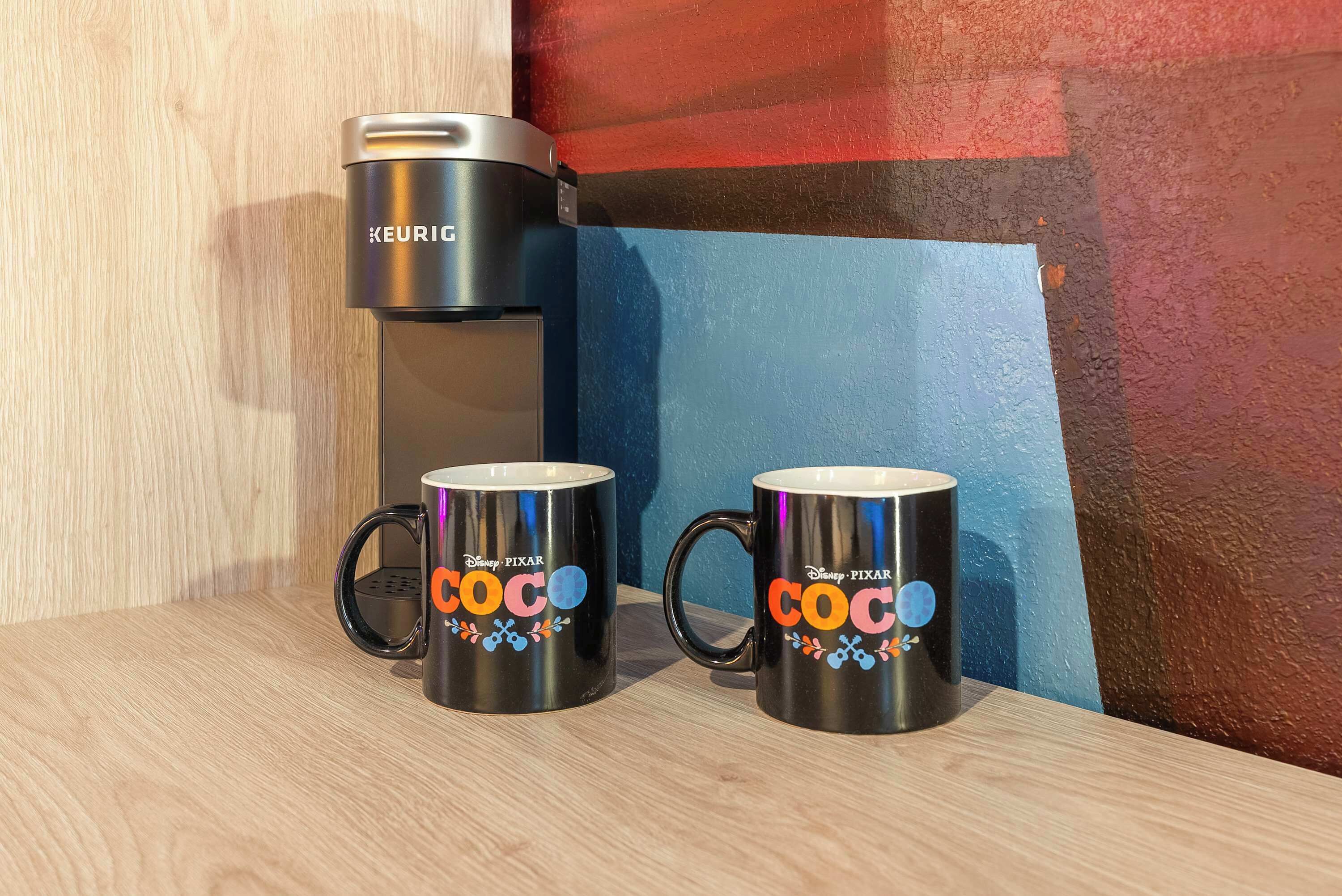Deux tasses noires ornées du texte « Disney Pixar Coco » et une machine à café Keurig, le tout posé sur une surface en bois.
