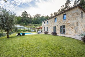 Ein Steinhaus mit Pool, einer überdachten Terrasse und einem Rasenstück.
