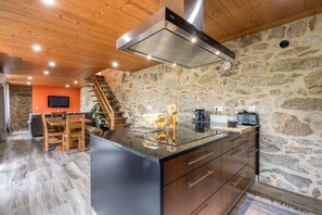 Eine moderne Küche mit einer Steinwand, Holzbalkendecke und einer Kochinsel mit Edelstahl-Dunstabzugshaube.