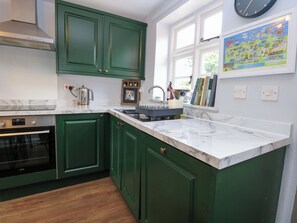 A kitchen with green cabinets, a marble countertop, a built-in oven, a sink, and a framed map on the wall. - The Mallows (Walsingham)
