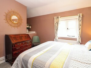 A bedroom with a bed, dresser, chair, window with curtains, and a wall-mounted mirror. - The Mallows (Walsingham)
