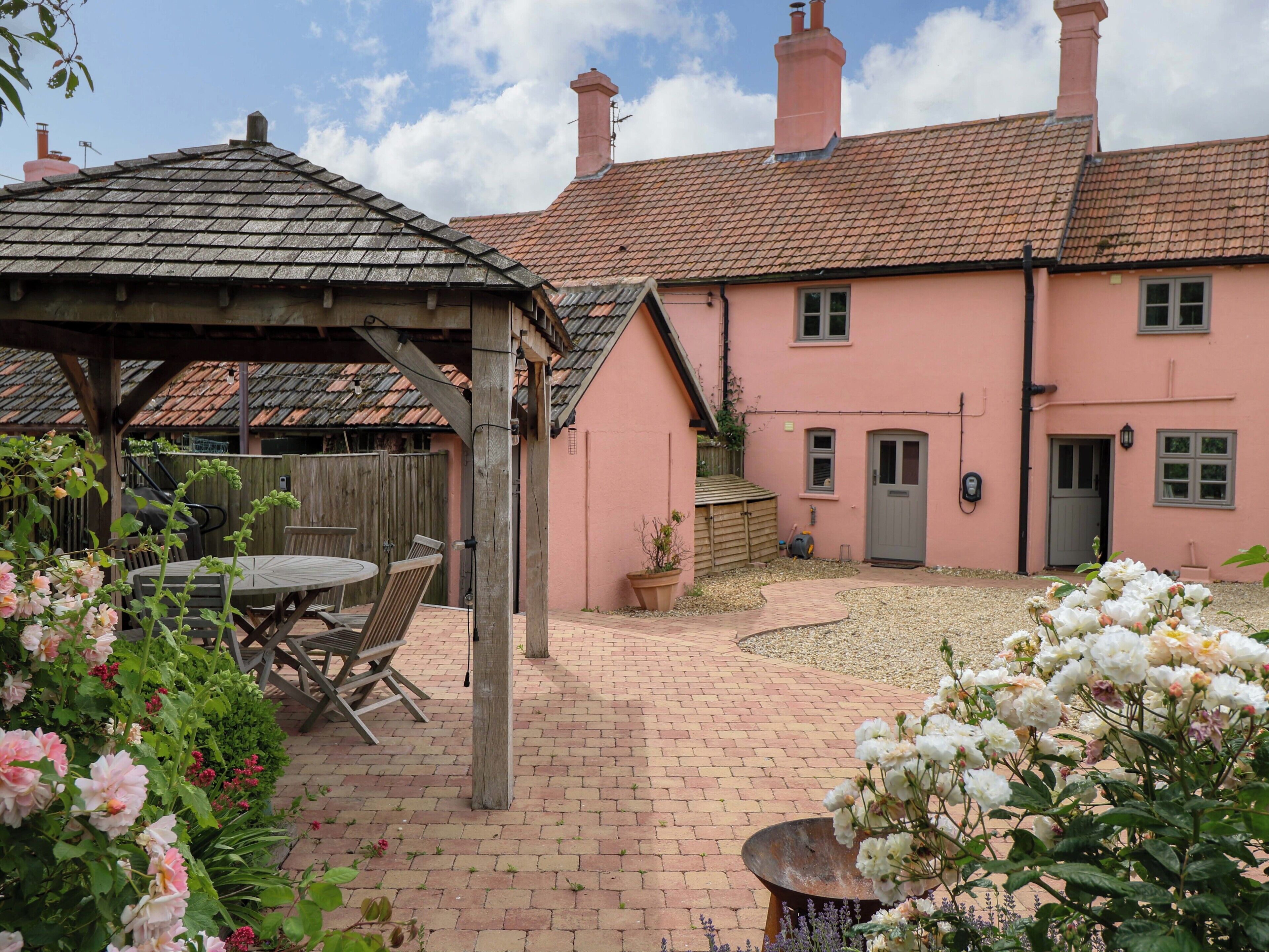 A pink house with a brick patio, a wooden pergola, and a garden with flowers.