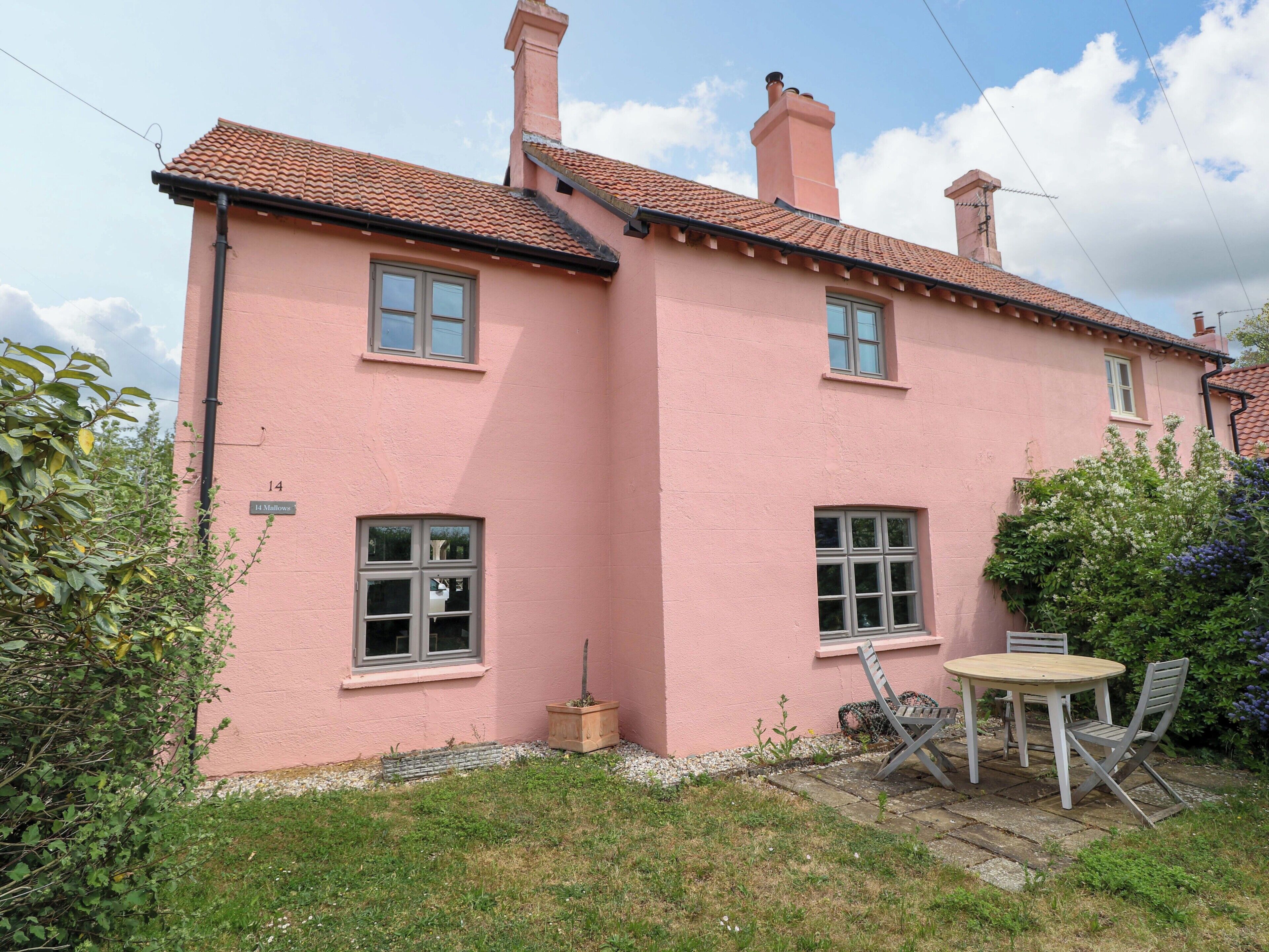 A pink house with a tiled roof, a small garden with a table and chairs, and a number '14' on the wall.