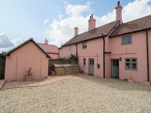 A pink house with a gravel driveway and a wooden fence. - The Mallows (Walsingham)