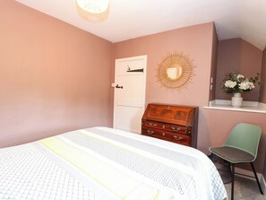 A bedroom with a bed, a dresser, a chair, a wall-mounted mirror, and a shelf with flowers. - The Mallows (Walsingham)