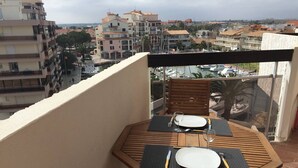 Varanda com mesa de madeira posta para dois, com vista para um porto e edifícios.