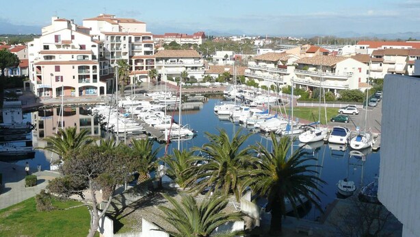 Uma marina com barcos atracados, rodeada por edifícios residenciais e palmeiras.