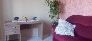 Ein Zimmer mit einem Holztisch, einem roten Sofa und einem weißen Strickkissen.