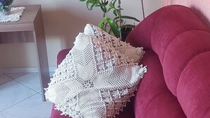 Un sofá rojo con un mantón blanco de crochet, una planta en maceta y un cuadro en la pared.