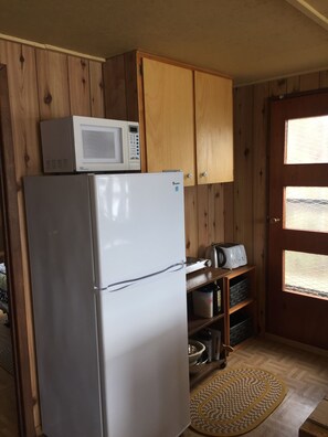 A compact kitchen with wooden cabinets, a refrigerator, a microwave, a toaster, and a small window. - Baysong Cottage, with Sauna, on Georgian Bay. (MacTier)