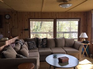 A cozy cabin interior with a sectional sofa, a round coffee table, and a lamp on a side table. - Baysong Cottage, with Sauna, on Georgian Bay. (MacTier)