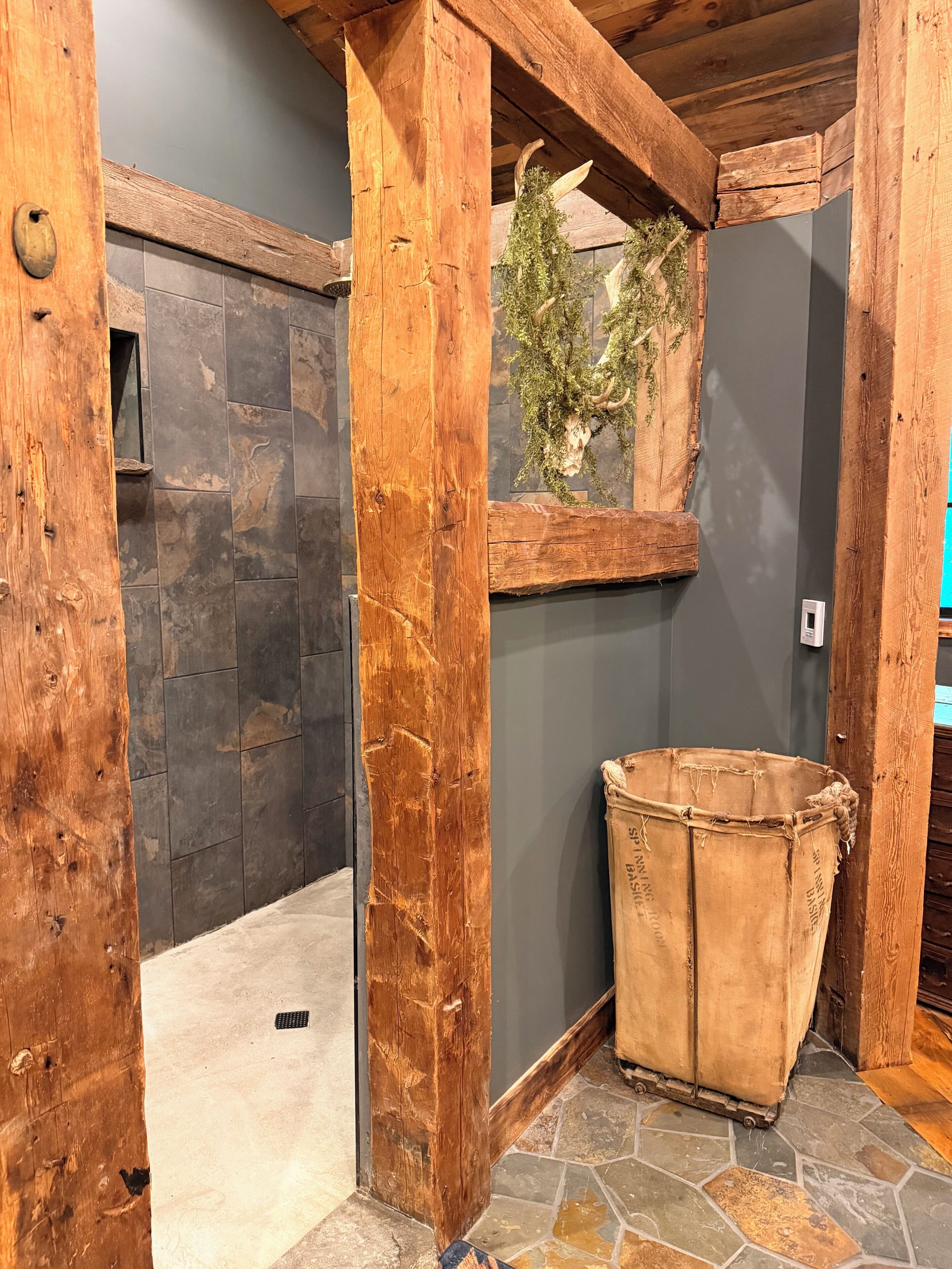 A rustic bathroom with a stone shower, wooden beams, and a rustic bucket.