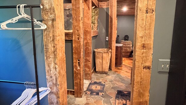 A hallway with wooden beams, a hanging clothes rack, a stone-tiled floor, and a door leading to another room.
