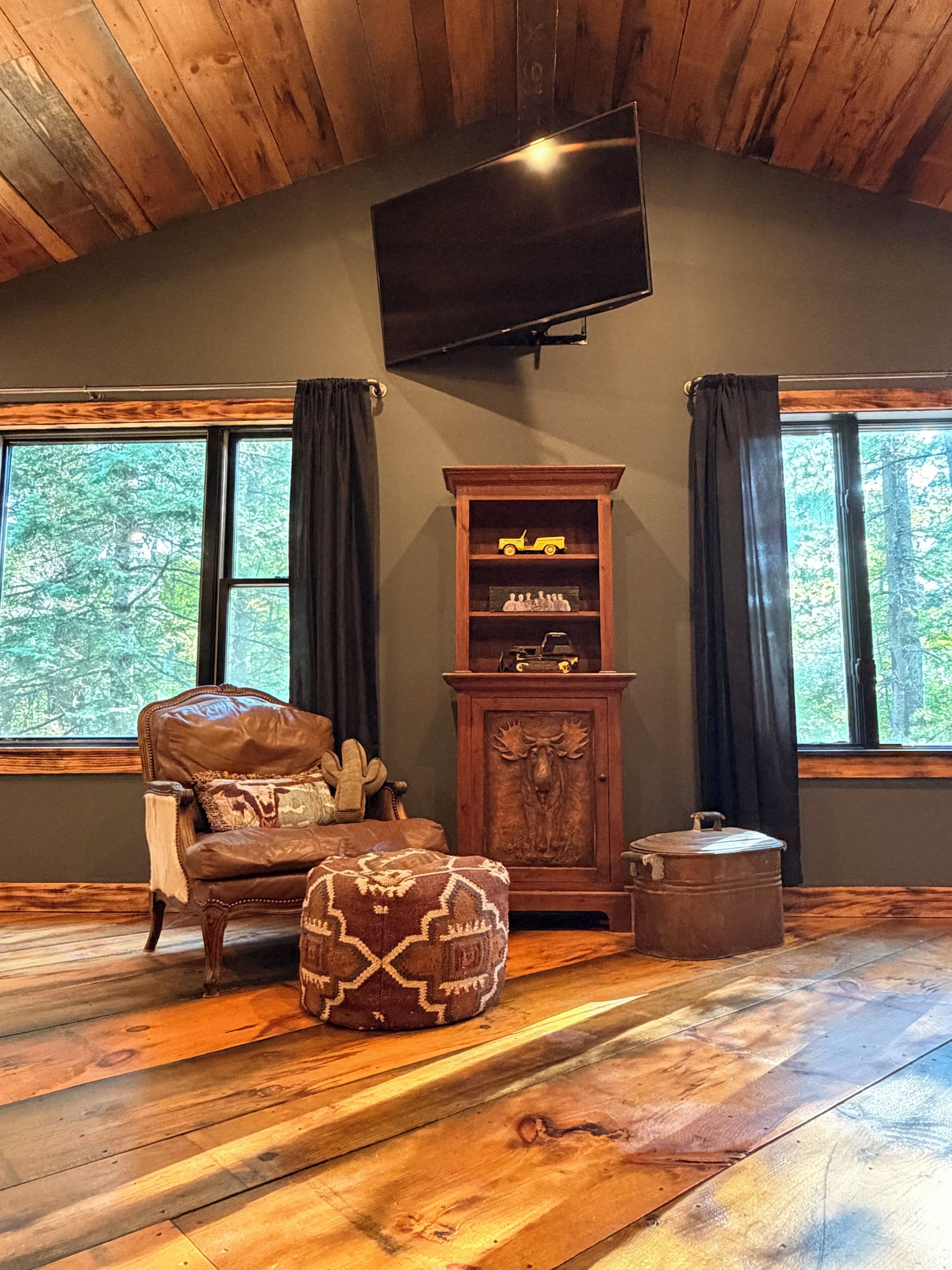 Ein Zimmer mit Ledersessel, Hocker, Holzschrank mit Dekoration und einem an der Wand montierten Fernseher.