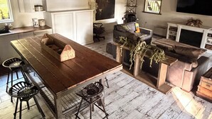 A rustic interior with a wooden dining table, bar stools, a sofa, and a television.