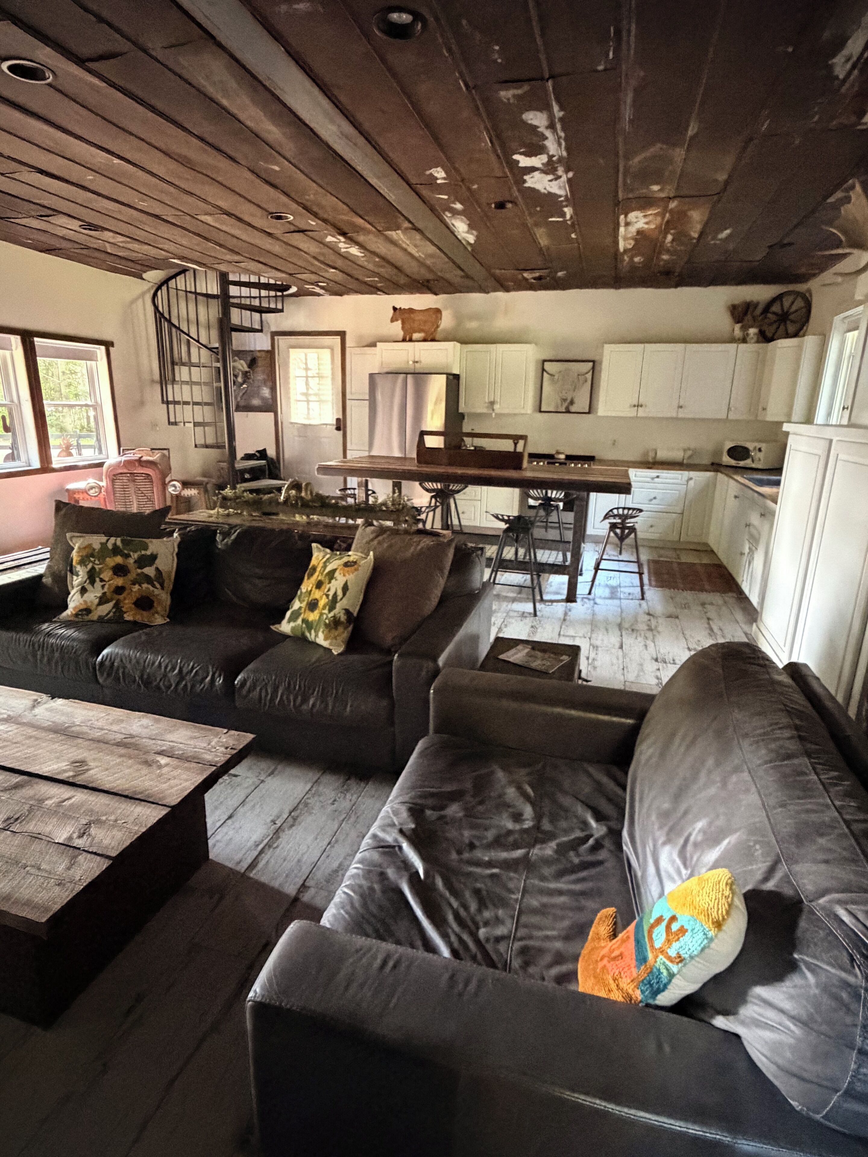 A rustic interior with a wooden ceiling, a dining area with a bar stool, and a kitchen with white cabinets.