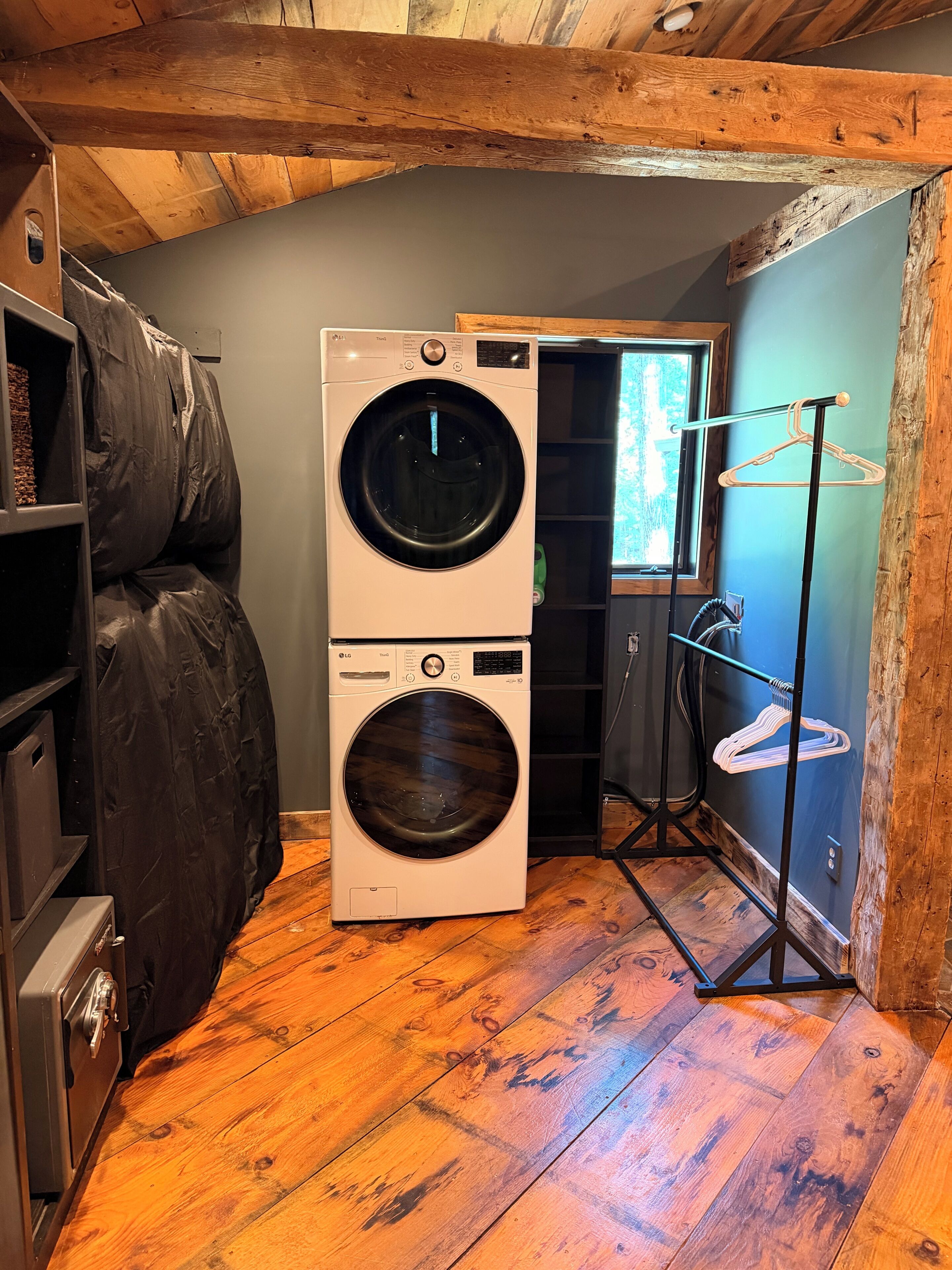 A laundry room with a stacked washer and dryer, wooden flooring, and a drying rack.