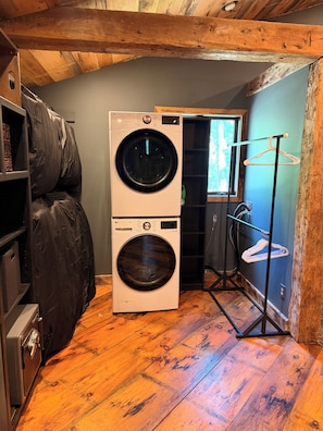 A laundry room with a stacked washer and dryer, wooden flooring, and a drying rack.