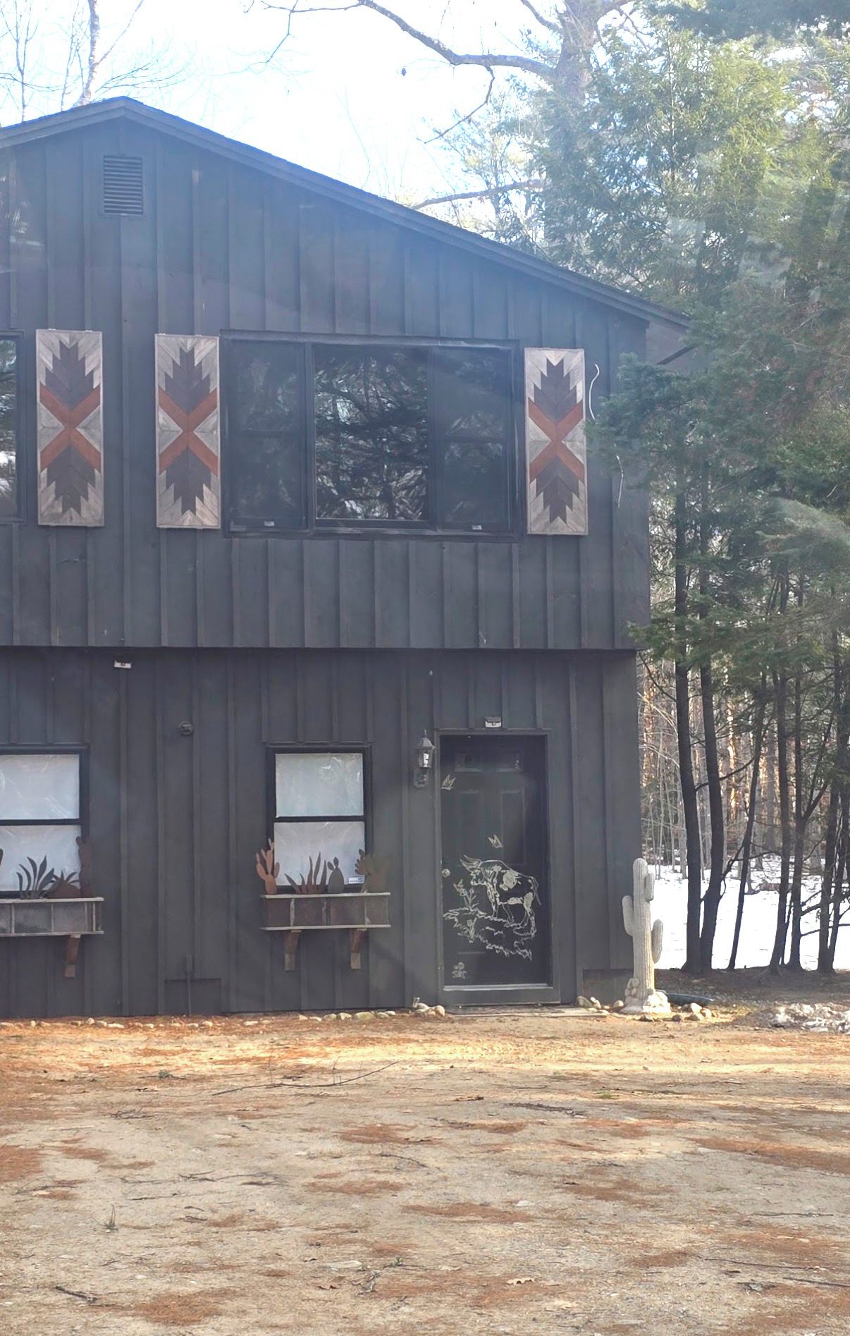 A two-story building with a metal exterior, a door with a cactus and a cow design, and three windows with decorative panels.