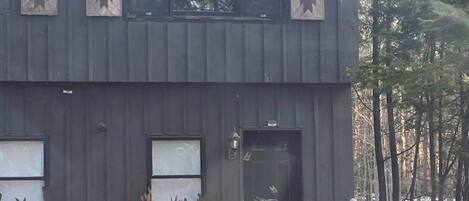 A two-story building with a metal exterior, a door with a cactus and a cow design, and three windows with decorative panels.