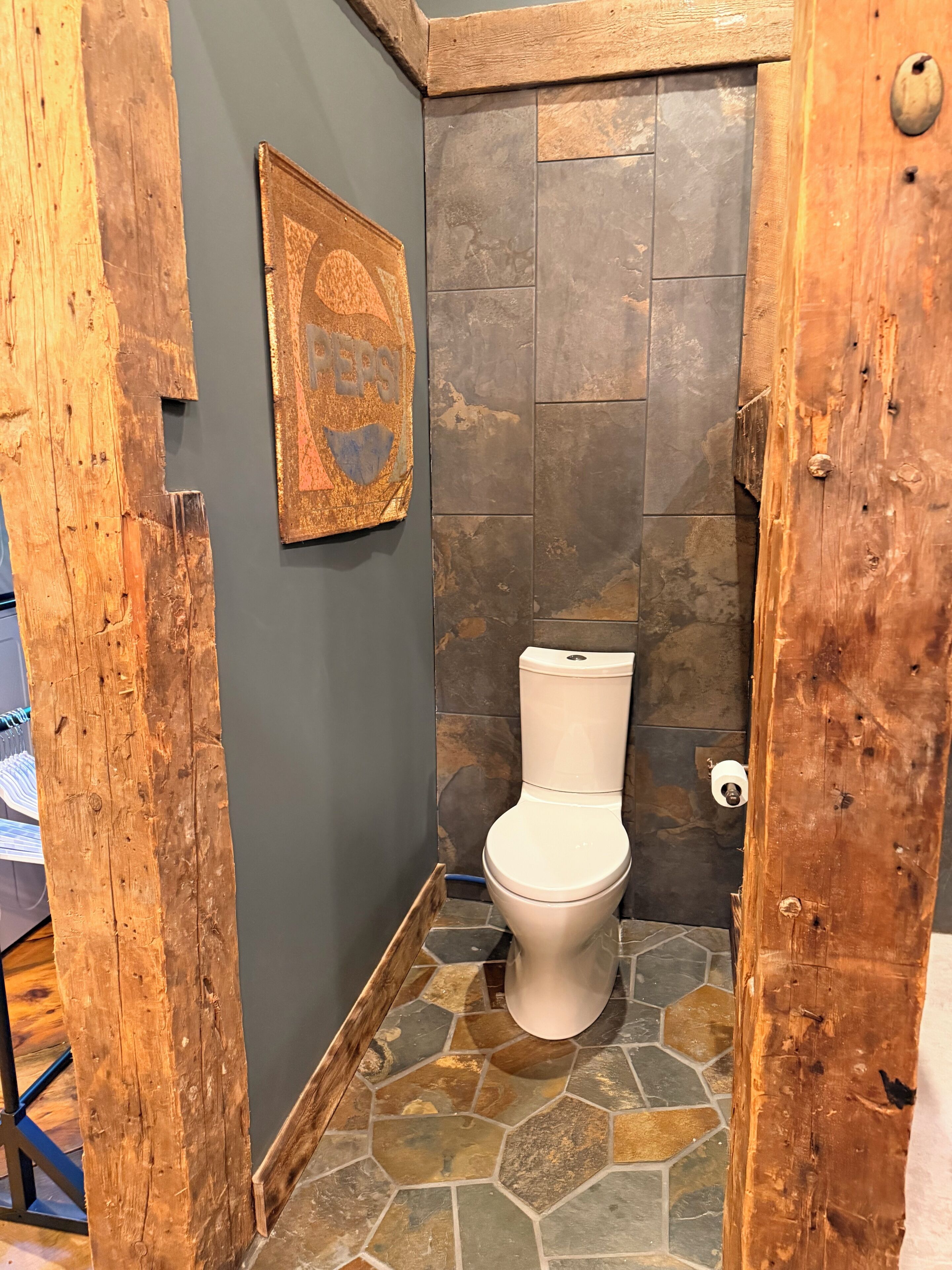Un baño con piso de baldosas de piedra, inodoro blanco y puerta de madera.