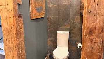 Un baño con piso de baldosas de piedra, inodoro blanco y puerta de madera.