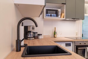 A modern kitchen with a black sink, stainless steel appliances, and a microwave above the counter. - Beautiful 3-bedroom Apartment 'Johann' (Stendal)