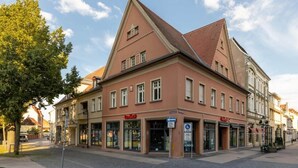 A traditional European building with a prominent gabled roof, storefronts on the ground floor, and a clear sky. - Beautiful 3-bedroom Apartment 'Johann' (Stendal)