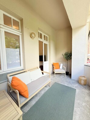 A covered patio with a wooden bench, a cushioned sofa, and a chair.