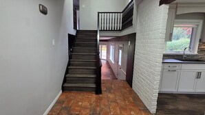 Escadaria que dá para um segundo andar com vista para um jardim, uma cozinha com armários brancos e um termostato na parede.