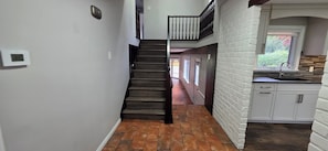 A staircase leading to a second floor with a view of a garden, a kitchen with white cabinets, and a thermostat on the wall. - Cottage Style living within city limit! (London)