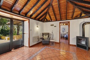 Una habitaci ón con suelo de baldosas, techo de madera, un sofá, una mesita, un radiador y una chimenea.