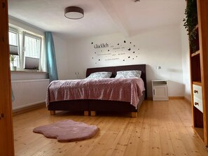 A bedroom with a bed, a bedside table, a wall decoration, and a window with curtains.