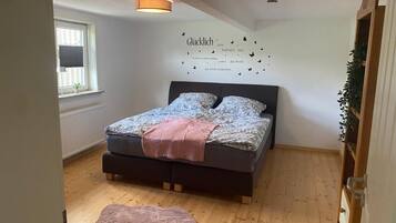 Ein Schlafzimmer mit einem Bett, einer Wandleuchte, einem Fenster mit Jalousien und einer kleinen Pflanze auf einem Regal.