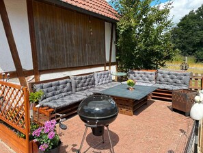 Un patio exterior con una parrilla, asientos acolchados y una mesa de madera.