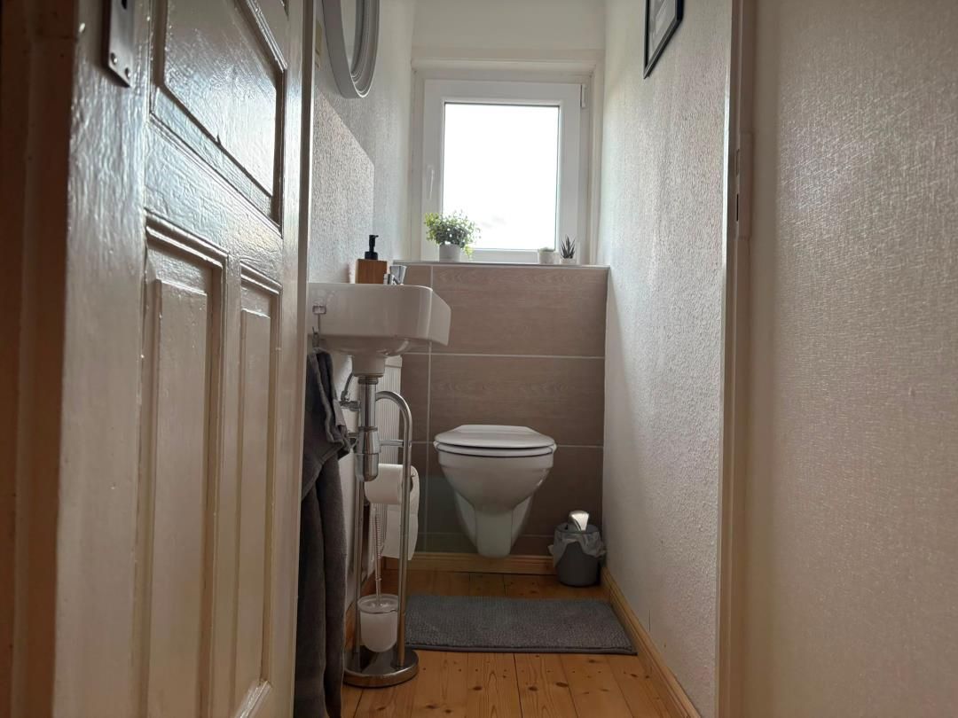 A narrow hallway leading to a bathroom with a toilet, sink, and window.