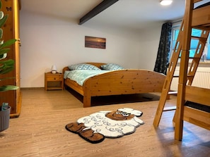 A bedroom with a wooden bed, a nightstand, a lamp, a window with curtains, and a wooden ladder. - NEW! Bruno vacation apartment (Gersfeld)
