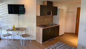 A compact living space with a kitchenette, a dining area with chairs, a bed, and a television mounted on the wall. - NEW! Vacation apartment Nino (Rötz)