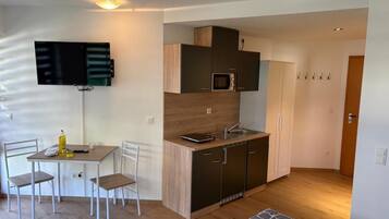 Un espace de vie compact comprenant un coin cuisine, un coin repas avec des chaises, un lit et un téléviseur fixé au mur.