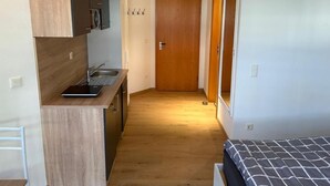 A compact kitchen with a microwave, sink, and wooden cabinets. A bed with a patterned bedspread is visible in the foreground. - NEW! Vacation apartment Nino (Rötz)