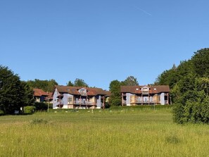 A row of two-story buildings with balconies, set in a grassy field with trees in the background. - NEW! Vacation apartment Nino (Rötz)