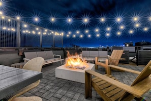 A rooftop patio with outdoor seating, a fire pit, and string lights. - Luxury Downtown Views - Rooftop - Hot Tub - Garage (Nashville)
