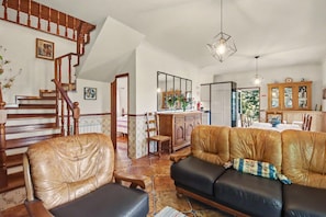 Ein Wohnzimmer mit Holztreppe, Ledersofas, einer Essecke und einer Küche.