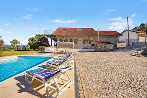 A stone building with a tiled roof, a swimming pool with lounge chairs, and a paved area. - Casa da Aldeia - Vale de Cambra (Arões)