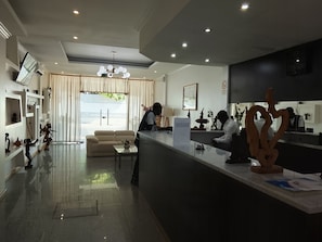 Un hall dâhĂŽtel moderne avec un comptoir dâaccueil, un espace salon et une grande fenĂȘtre agrĂ©mentĂ©e de rideaux.