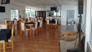 A spacious dining area with wooden tables and chairs, a kitchen area with a counter and sink, and a television mounted on the wall. - Hotel P.B (Benguela)