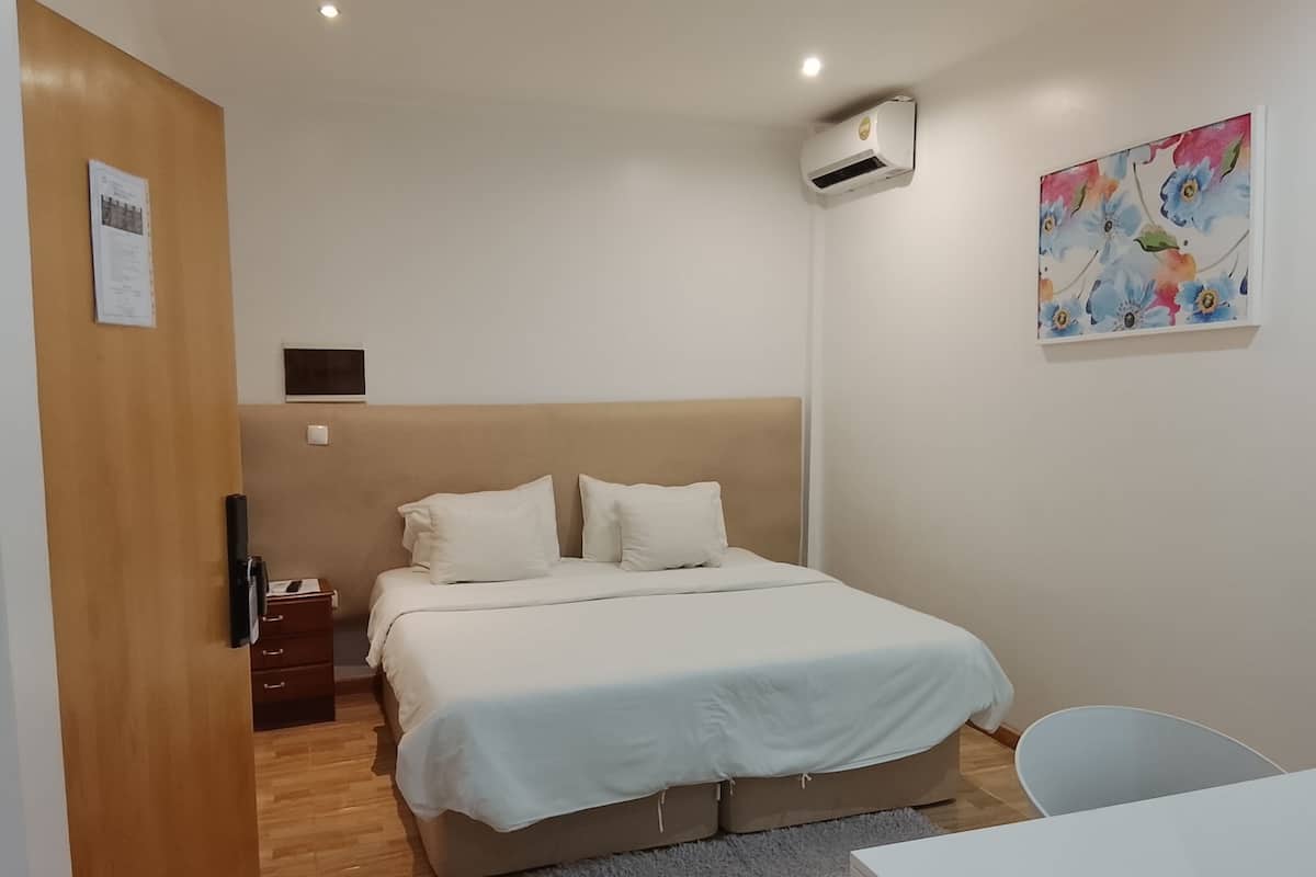 Un dormitorio con cama, mesita de noche, equipo de aire acondicionado y un cuadro en la pared.