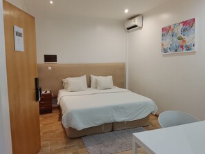 A bedroom with a bed, bedside table, air conditioning unit, and a painting on the wall.