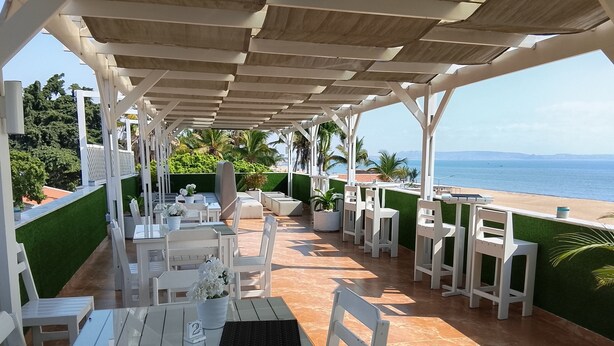 An outdoor patio with white furniture, a glass table, and a view of the sea. - Hotel P.B (Benguela)