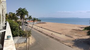A beach view with a road, palm trees, and a distant mountain range. - Hotel P.B (Benguela)